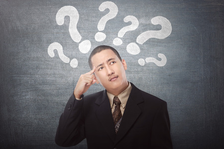 Young asian businessman confused with question marks above his head on black backgroundの写真素材