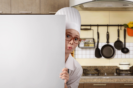 Young asian woman chef standing from behind white board on kitchen roomの写真素材