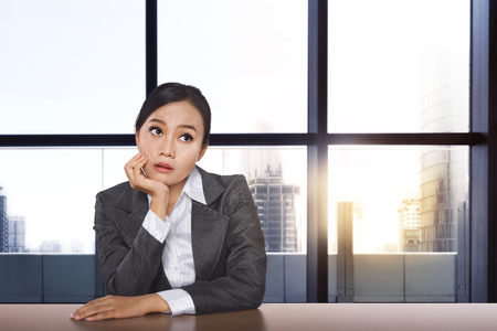 Stressed asian businesswoman thinking the solution while working with glasses window backgroundの写真素材