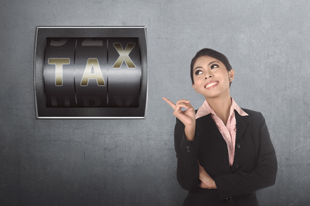 Beautiful asian business woman pointing counter digit with tax sign on behind herの写真素材