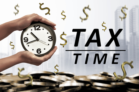 People hand holding alarm clock beside Tax time message on modern backgroundの写真素材