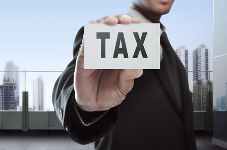 Businessman showing Tax text on white card at officeの写真素材