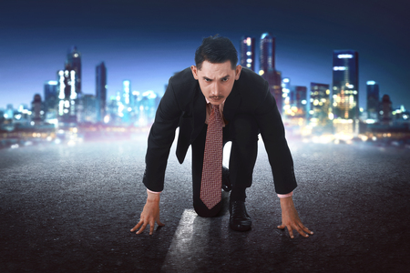 Young asian businessman in start position ready to race on concrete with city backgroundの写真素材