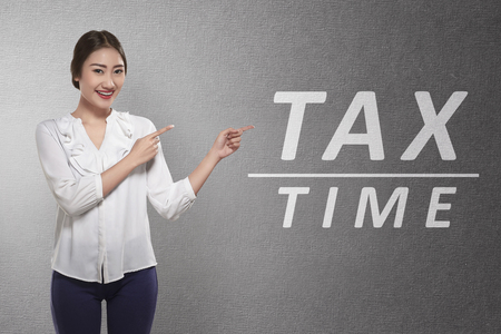 Beautiful asian business woman pointing Tax time word on the gray wallの写真素材