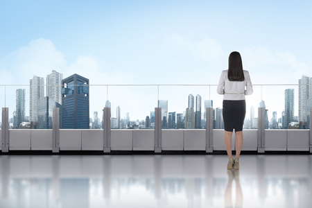Portrait of asian business woman standing on a terrace and looking at modern cityの写真素材