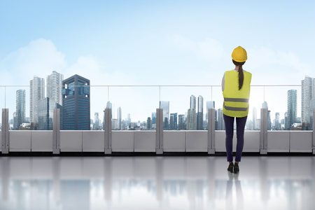 Portrait of asian woman with yellow helmet standing on terrace looking at cityscapeの写真素材
