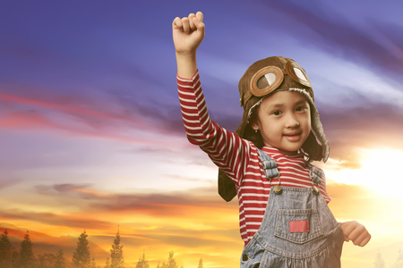 Beautiful asian child with pilot costume playing on the field at sunsetの写真素材
