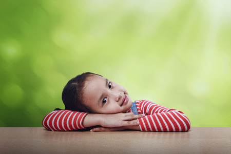Cheerful asian kid lying down on the table over green backgroundの写真素材