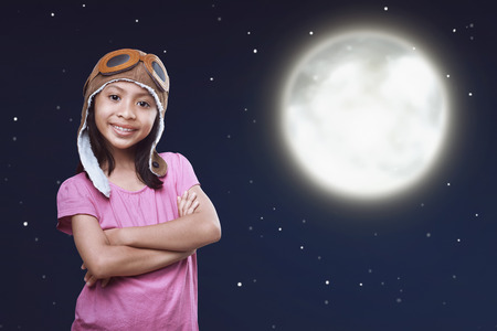 Cheerful asian child wearing aviator cap and googles standing on the moonlight at nightの写真素材