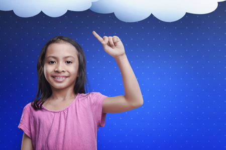 Happy asian child with a new idea in her head over blue backgroundの写真素材