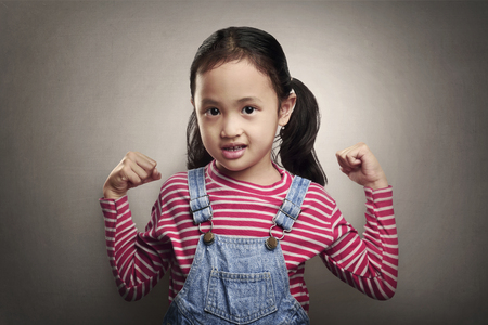 Attractive asian little girl showing her muscle on grey backgroundの写真素材