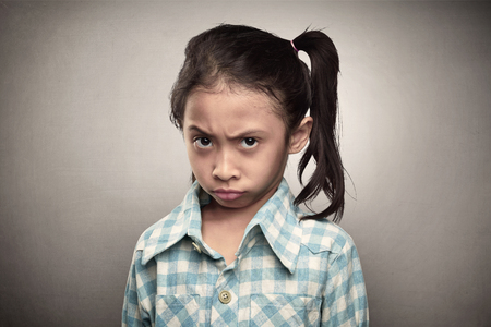 Depressed asian child showing her unhappy face over grey backgroundの写真素材