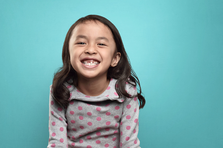 Smiling asian little girl and her broken teeth over blue backgroundの写真素材