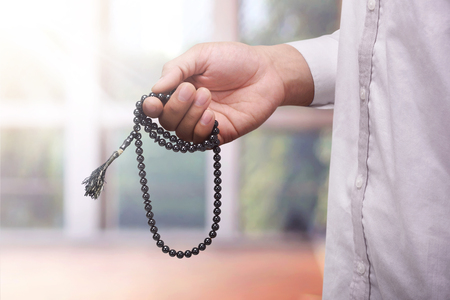 Hand of muslim man praying while holding tasbih against blurred backgroundの写真素材