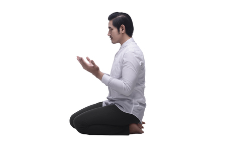 Religious asian muslim man sitting while praying isolated over white backgroundの写真素材