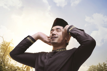 Young asian muslim man with black cap pray at sunsetの写真素材