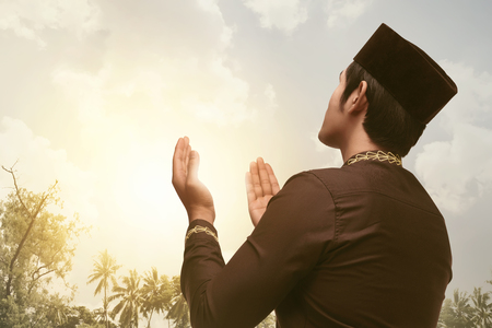 Devout asian muslim man praying with his both hands with sunset backgroundの写真素材