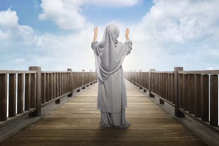 Back view of asian muslim girl standing and praying to god with blue sky backgroundの写真素材