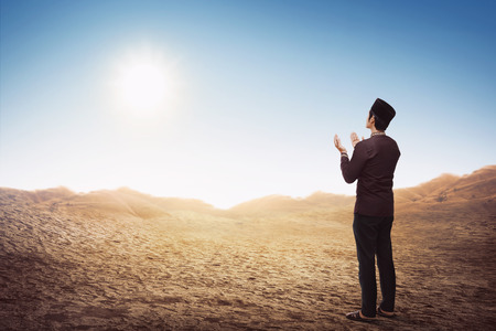 Back view of asian muslim man standing and praying in the desertの写真素材