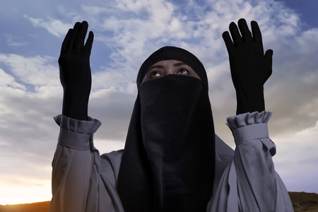 Religious asian muslim woman with hijab raising hand and praying against sky backgroundの写真素材