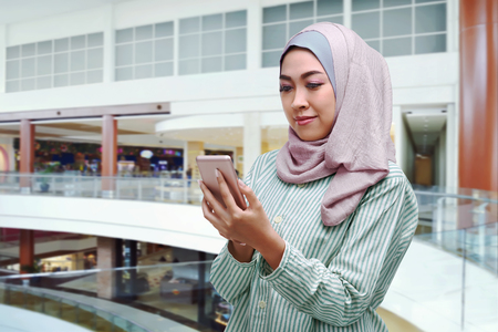Young asian muslim woman in veil using mobile phone in the mallの写真素材