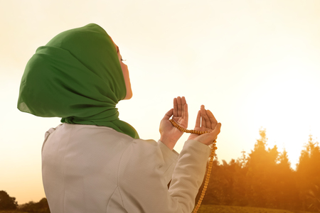 Beautiful asian muslim woman praying with prayer beads during sunsetの写真素材