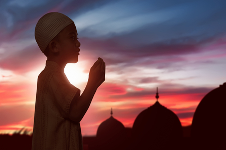 Portrait of asian muslim child raising hand and praying over sunset backgroundの写真素材