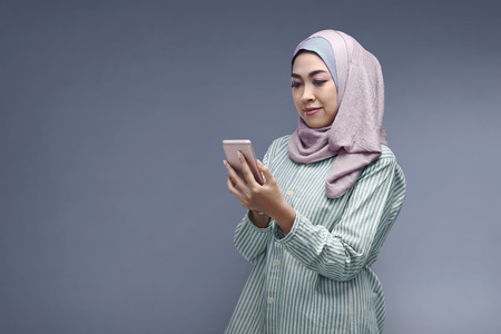 Young asian muslim woman in hijab with her smartphone over dark backgroundの写真素材