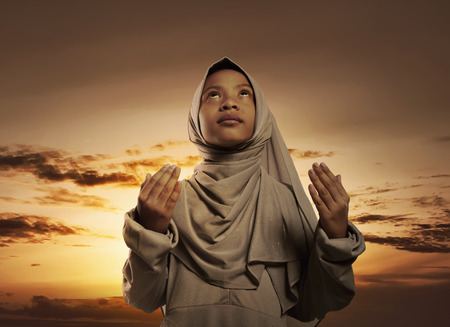 Little asian muslim girl with hijab praying to god over sunset backgroundの写真素材