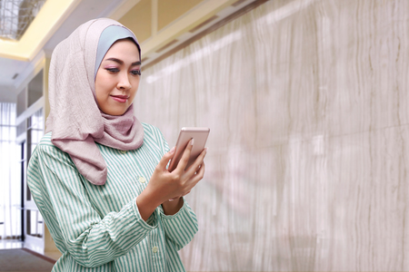 Beautiful asian woman with hijab holding smartphone at officeの写真素材