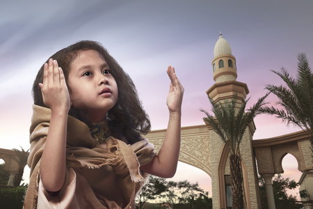 Little asian muslim girl raising hand and praying with sunset backgroundの写真素材
