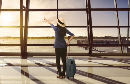 Traveler asian woman with suitcase looking sunset through window at terminal airportの写真素材