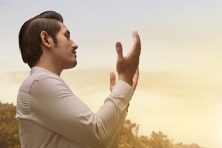 Handsome asian muslim man with traditional dress praying during sunsetの写真素材