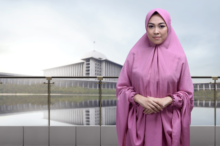 Religious asian muslim woman wearing veil with clasping hand standing against mosque backgroundの写真素材