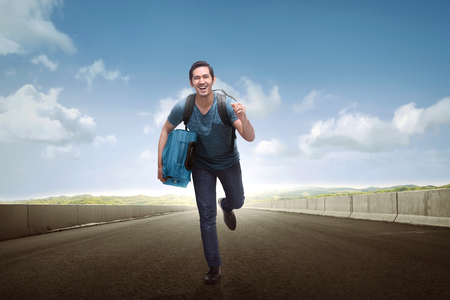 Happy asian tourist man carrying luggage running along the streetの写真素材