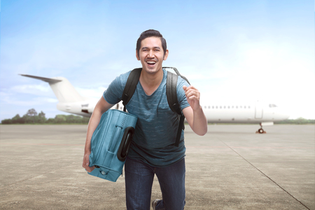Young asian travelling man get off the plane with suitcase on the landing stripの写真素材