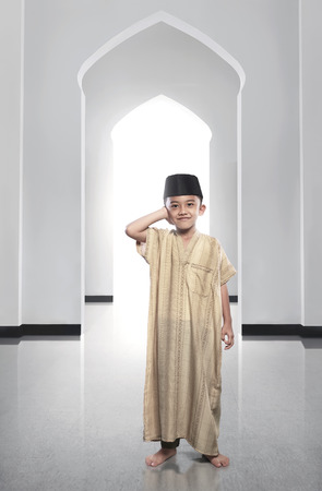 Cheerful asian muslim kid wearing traditional dress praying on the mosqueの写真素材