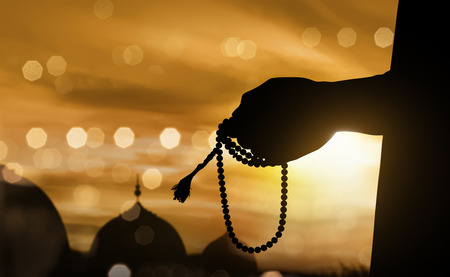 Silhouette muslim man praying with prayer beads during sunset backgroundの写真素材