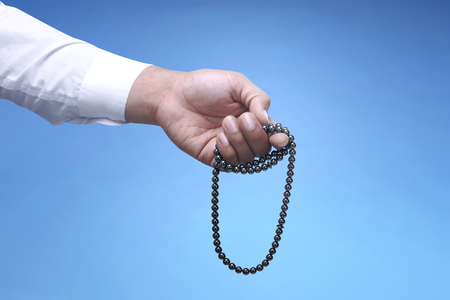 Muslim man praying with prayer beads over blue backgroundの写真素材