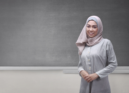 Portrait of asian muslim woman wearing veil standing against blackboard backgroundの写真素材