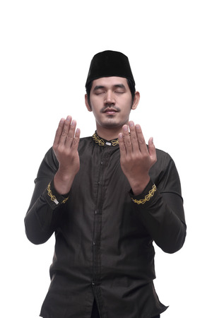 Young asian muslim man with cap praying isolated over white backgroundの写真素材