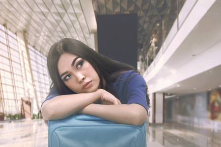 Beautiful asian tourist with sleepy expression on suitcase at airport terminalの写真素材