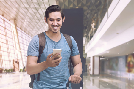 Happy asian tourist holding phone and suitcase in the airportの写真素材