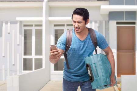 Portrait of asian traveler man running carrying suitcase with home at backgroundの写真素材