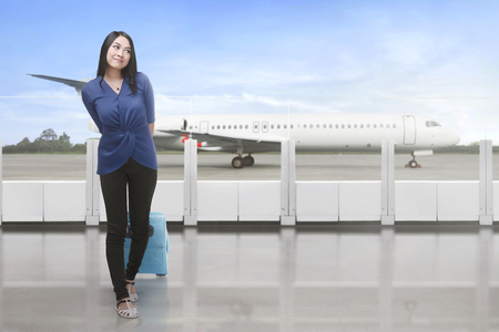 Portrait of asian traveler carrying suitcase waiting plane at airportの写真素材