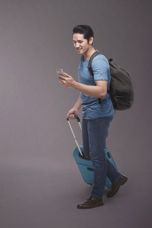 Traveler asian man with backpack using smartphone over dark backgroundの写真素材