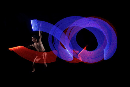 Young man ballet dancing with blue and red lights effect agaisnt black backgroundの写真素材