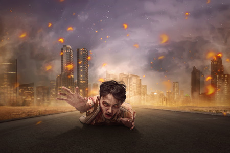 Aggressive asian bloody zombie man crawling from burning cityの写真素材