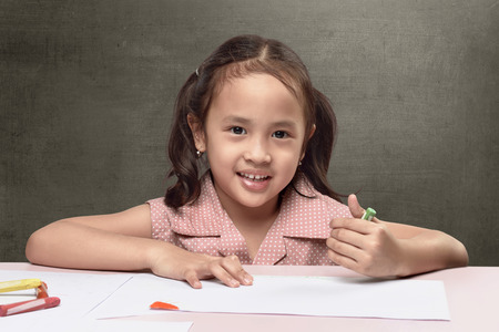 Cute asian little girl drawing on white paper against blackboard backgroundの写真素材