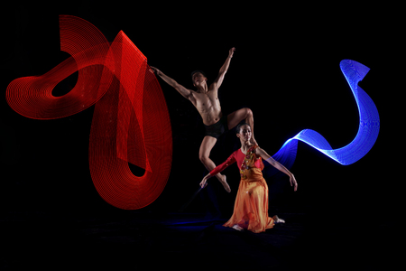 Portrait of couple ballet dancing with motion lights effect over black backgroundの写真素材